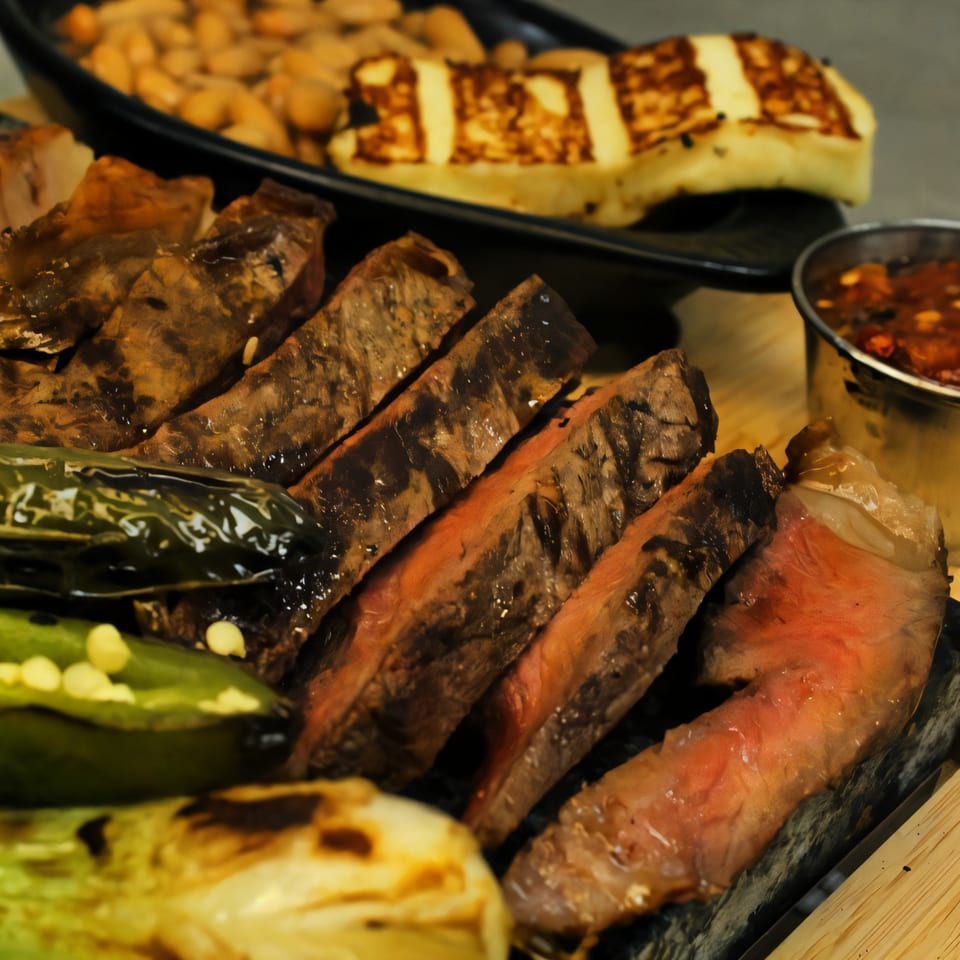 Sliced grilled steak, charred jalapeños, and grilled onions with beans and cheese in the background.