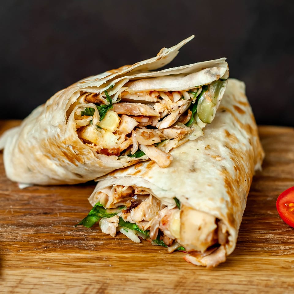 Two chicken shawarma wraps, cut in half, revealing chicken, lettuce, and sauce on a wooden board.